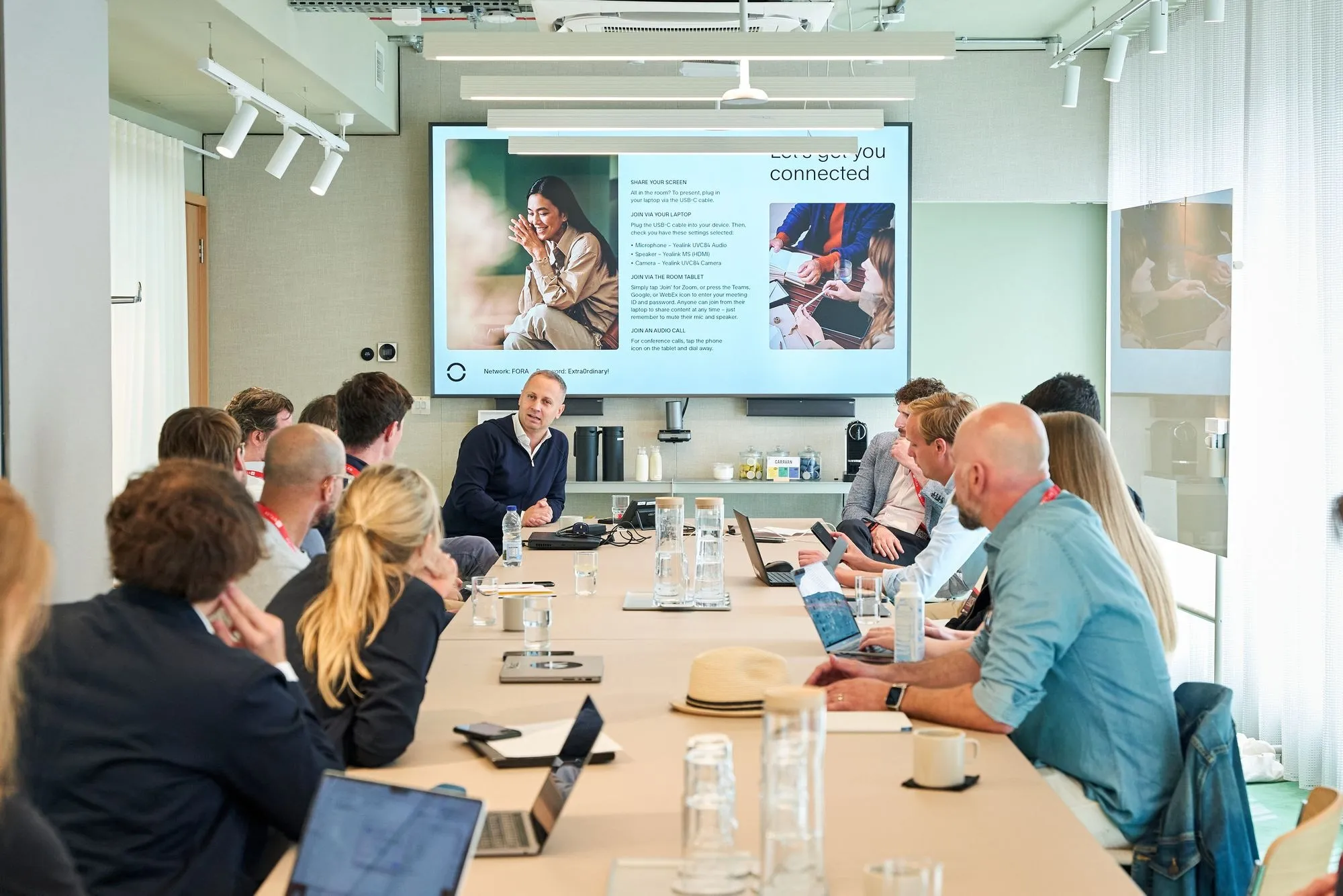 Founders around a table in a meeting room, watching a presentation and taking notes